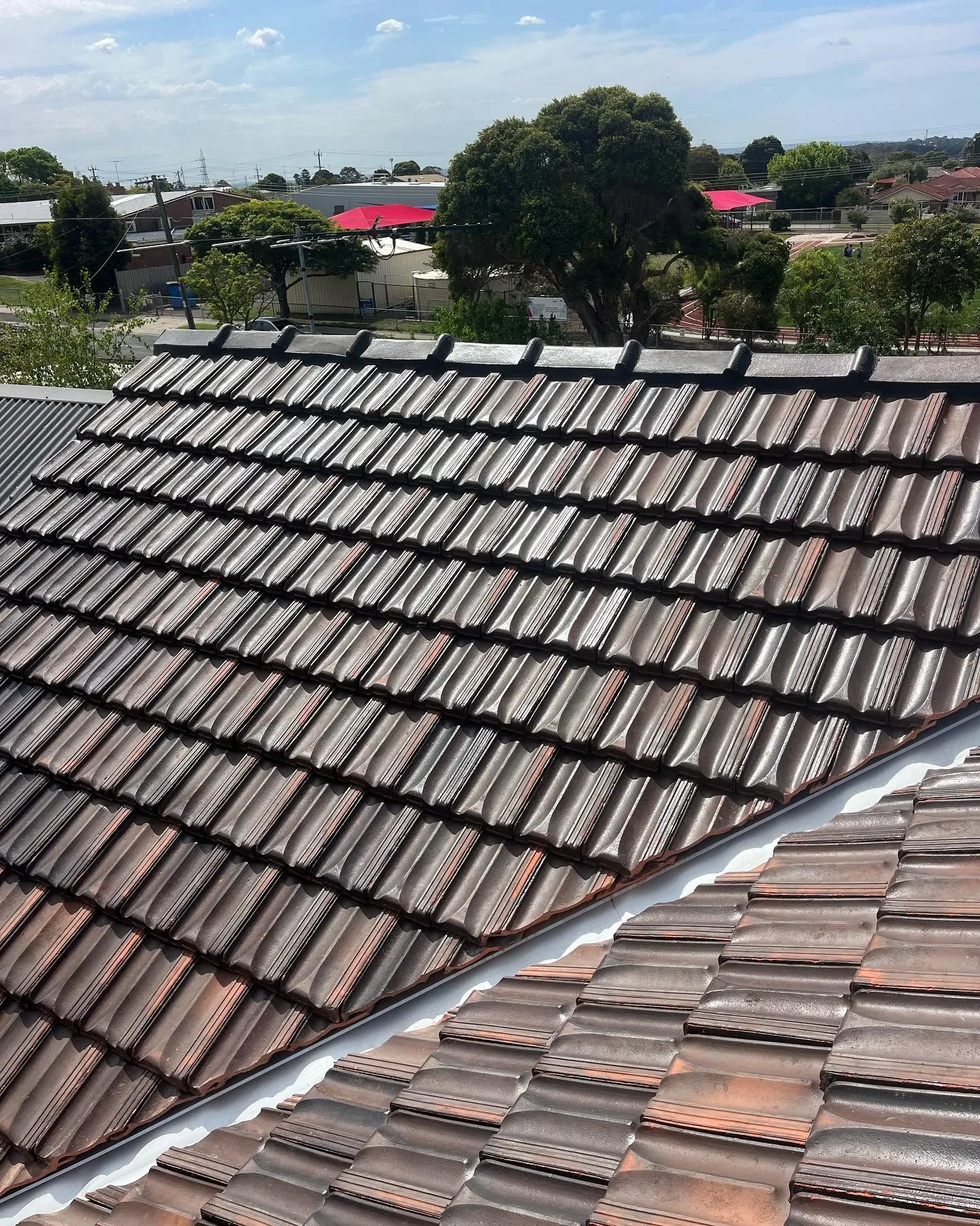 Close-up of a glazed terracotta roof valley showing clean, re-pointed tiles on one side against still-unwashed tiles on the other