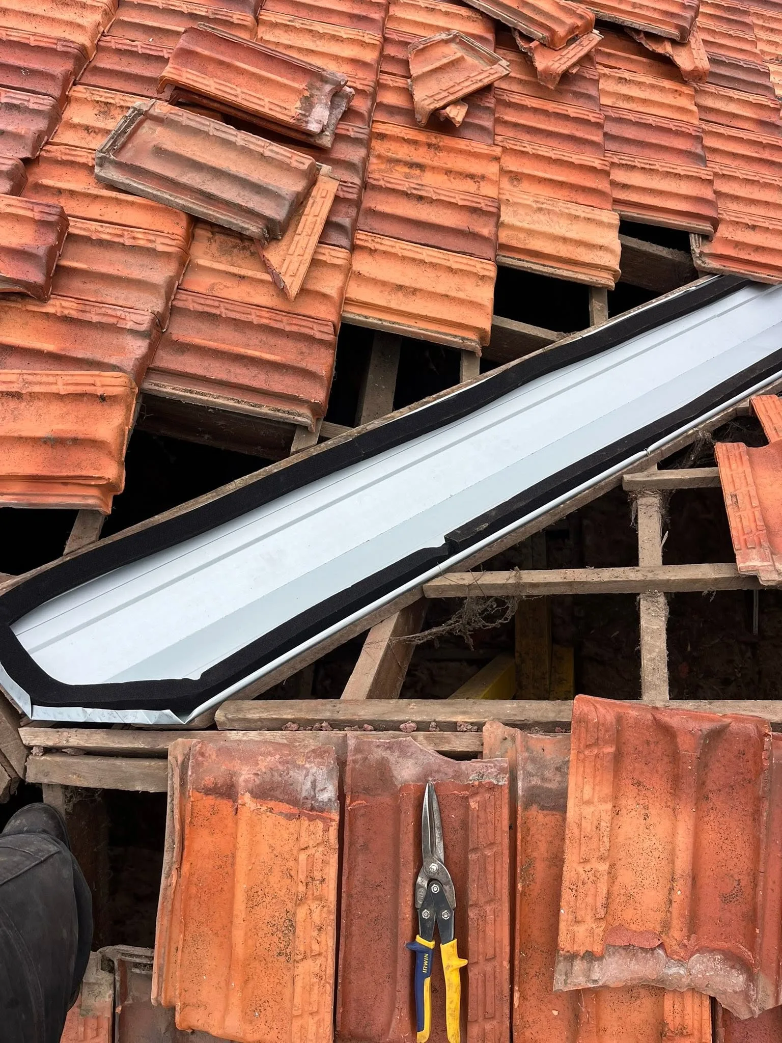 Close-up of a new metal valley being installed in a terracotta tile roof, with tiles pulled back to expose the roof frame